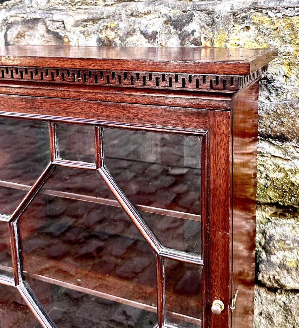 A dark mahogany Victorian wall cupboard featuring a carved Greek key frieze and a single astragal glazed door with an octagonal central glass pattern. View III