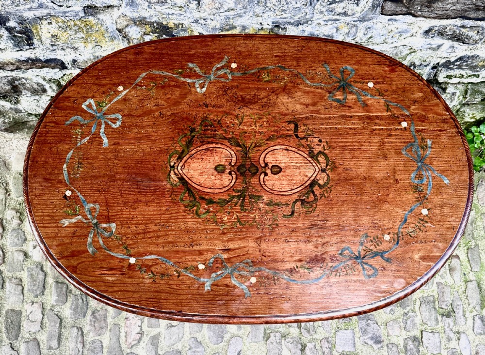 An oval wooden occasional table featuring hand-painted ribbon and floral garlands on the tabletop, supported by four tapered legs with linear details. View III