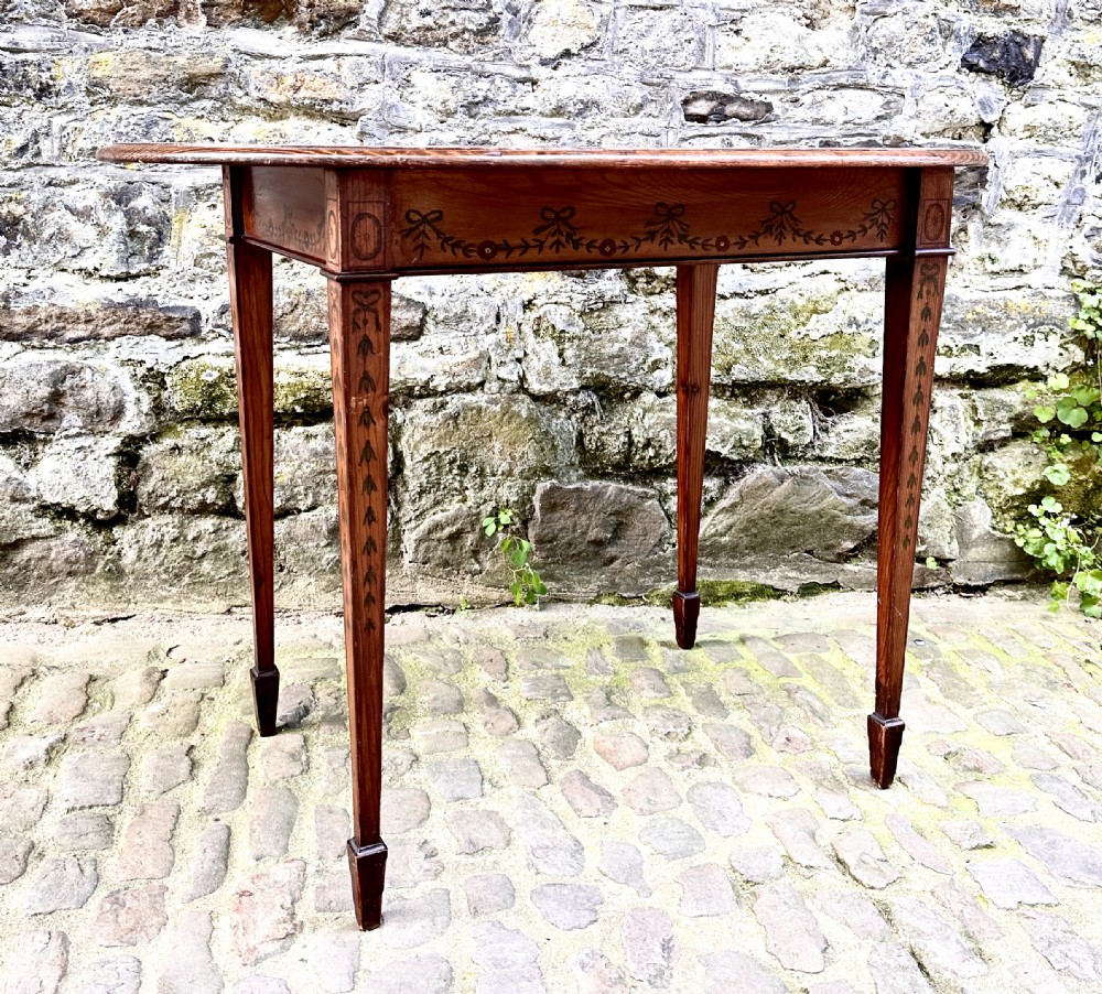 An oval wooden occasional table featuring hand-painted ribbon and floral garlands on the tabletop, supported by four tapered legs with linear details. View V
