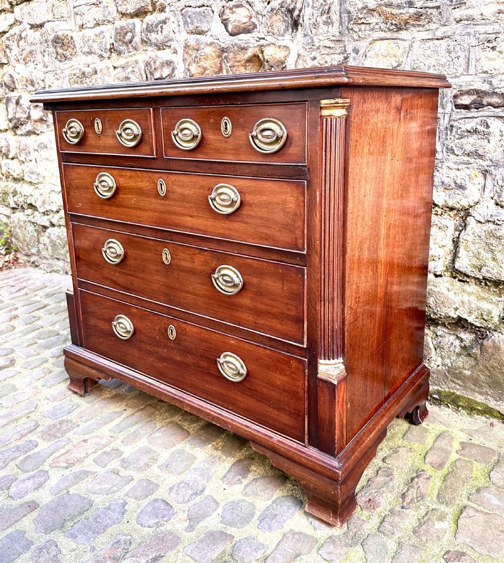A George III mahogany chest of drawers featuring two short over three long graduated drawers, brass oval handles, fluted corner columns, and bracket feet. View V