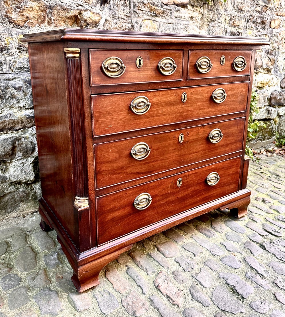 A George III mahogany chest of drawers featuring two short over three long graduated drawers, brass oval handles, fluted corner columns, and bracket feet. View VI