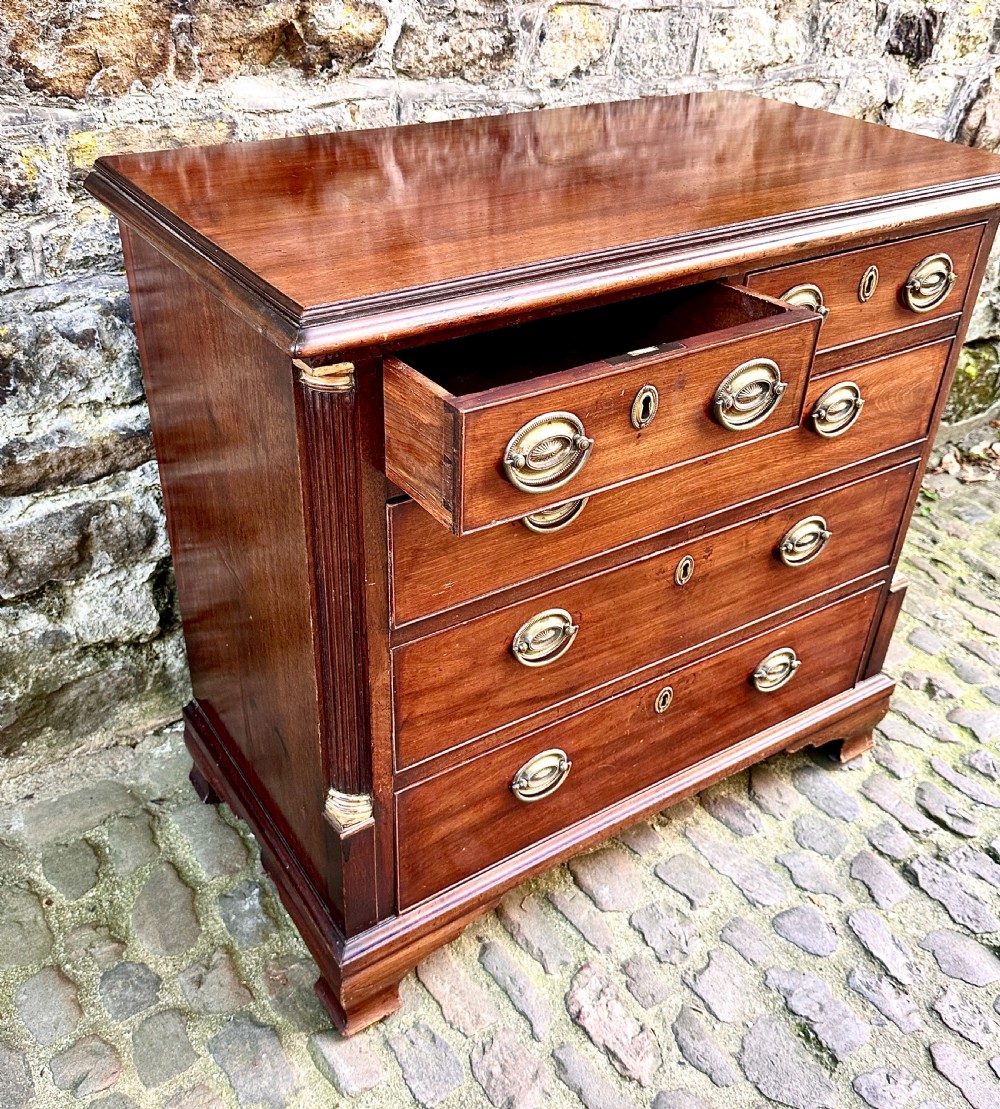 A George III mahogany chest of drawers featuring two short over three long graduated drawers, brass oval handles, fluted corner columns, and bracket feet. View VII