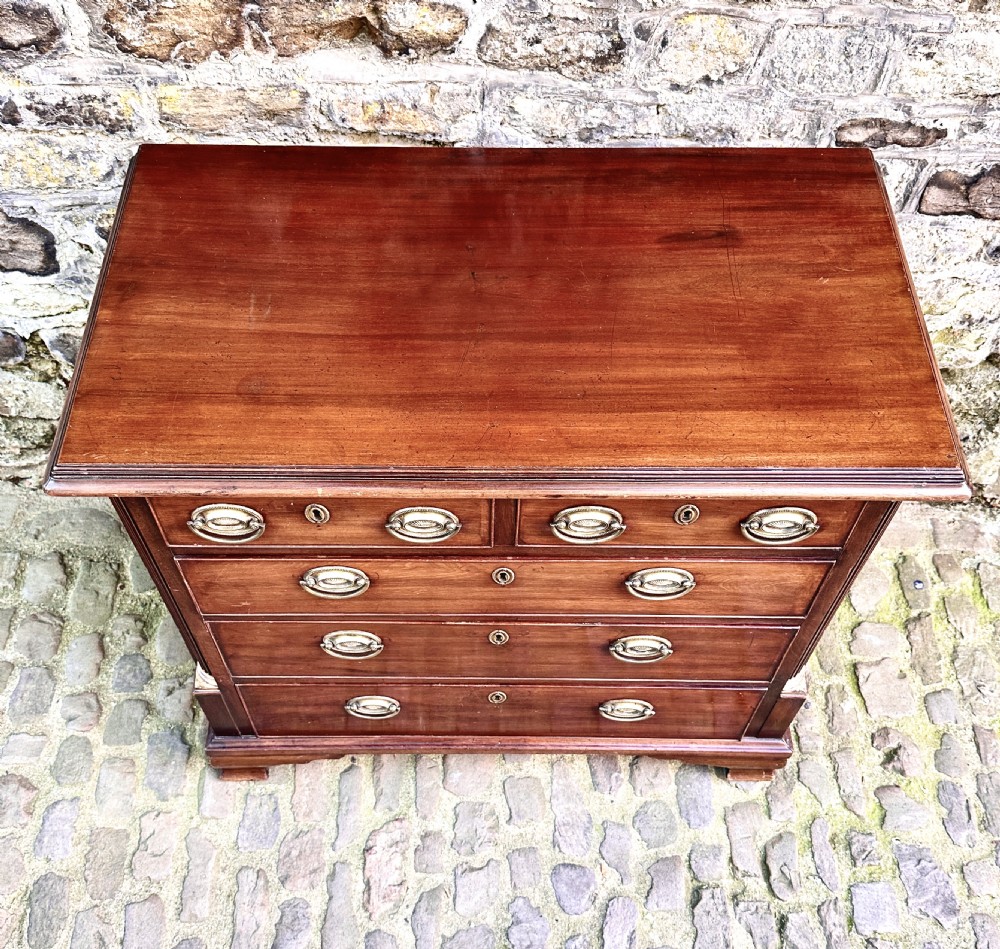 A George III mahogany chest of drawers featuring two short over three long graduated drawers, brass oval handles, fluted corner columns, and bracket feet. View IX