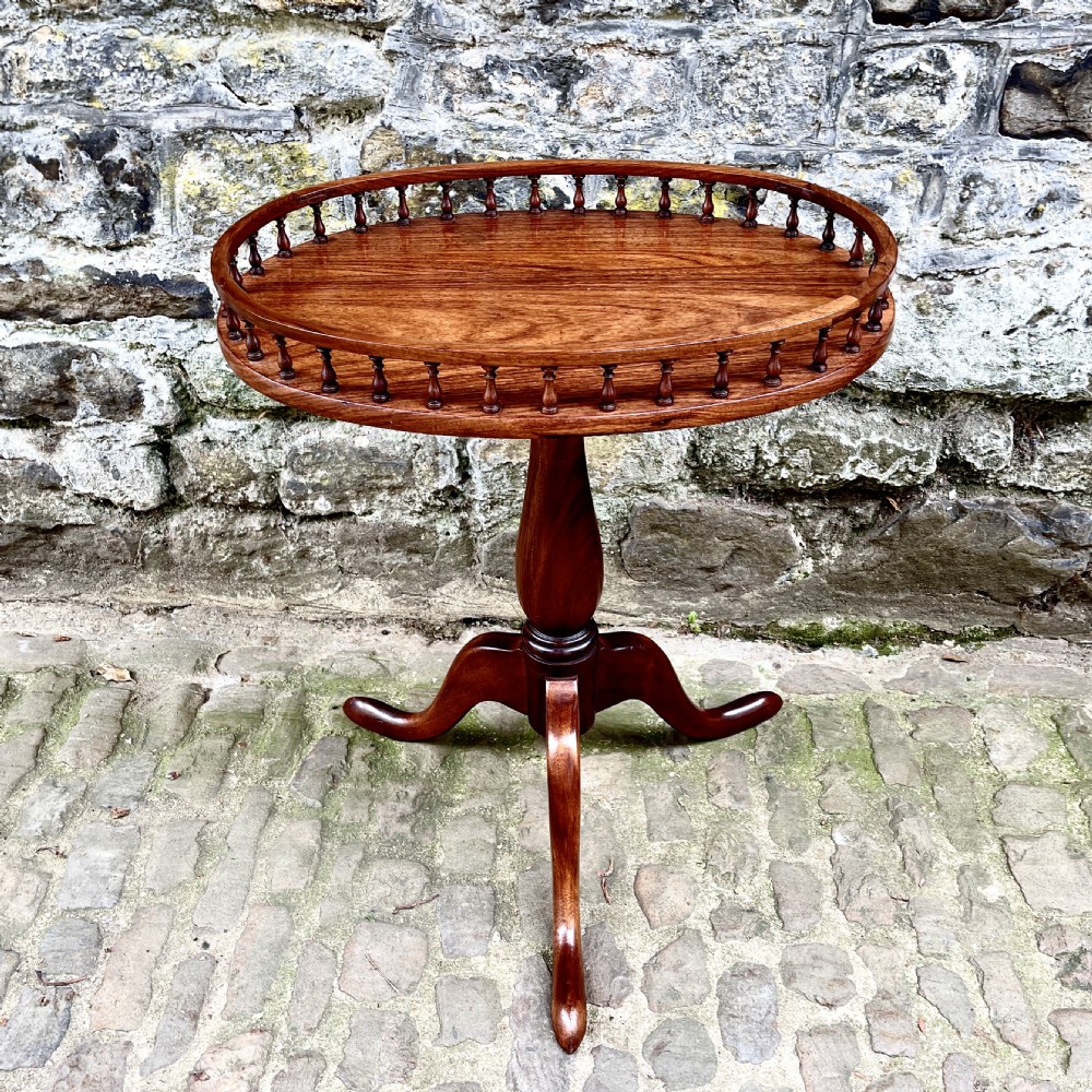 A late Victorian rosewood wine table featuring an oval top with a spindle gallery rail, raised on a central turned pedestal with tripod legs.