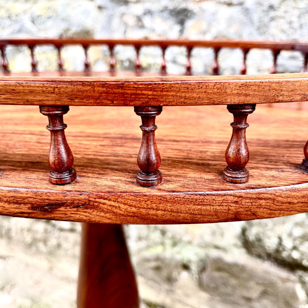 A late Victorian rosewood wine table featuring an oval top with a spindle gallery rail, raised on a central turned pedestal with tripod legs. View IV