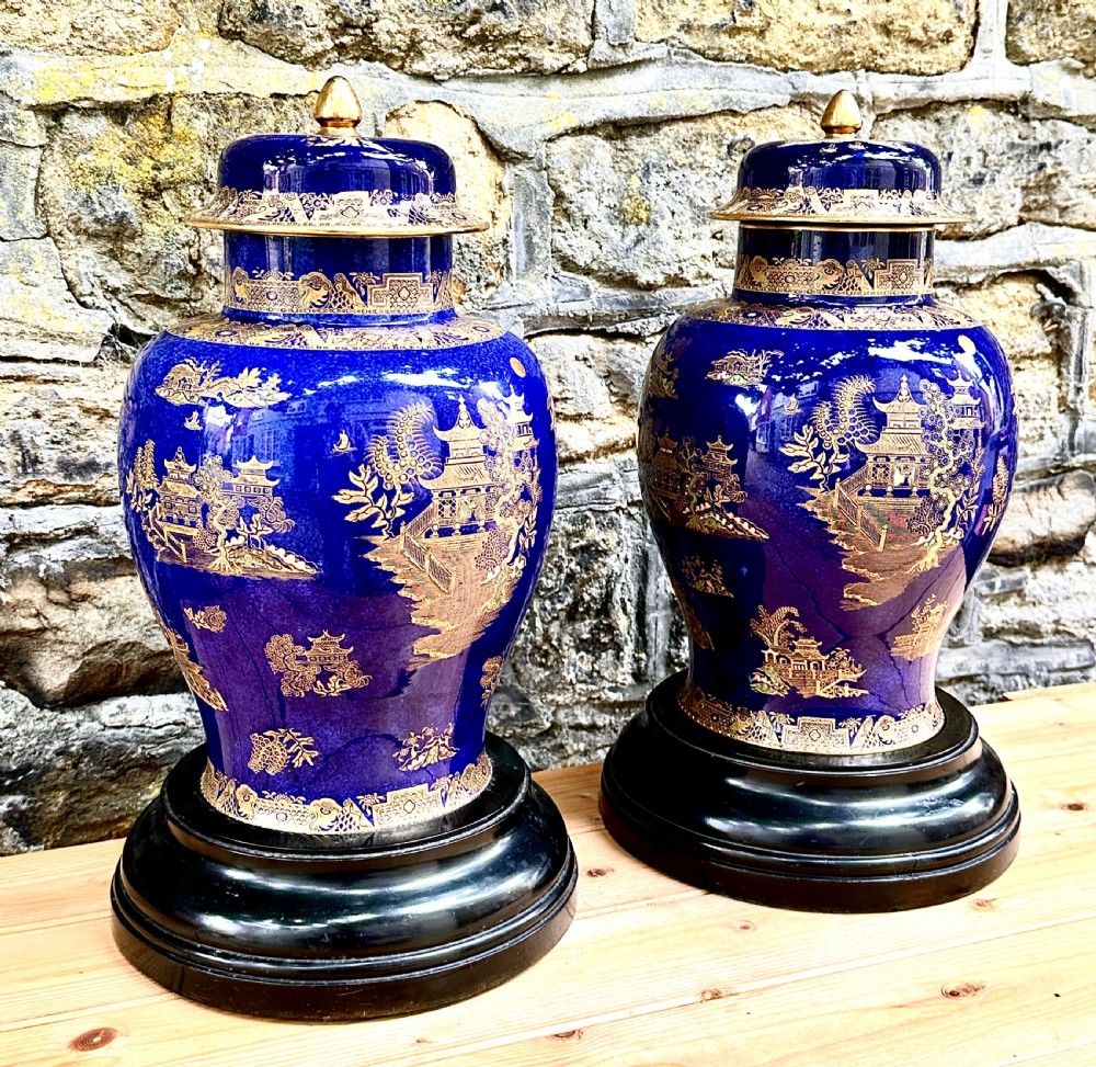 A pair of cobalt blue ceramic lidded vases decorated with gold gilt Chinoiserie pagoda scenes, set on dark circular ebonised wooden bases. View IV