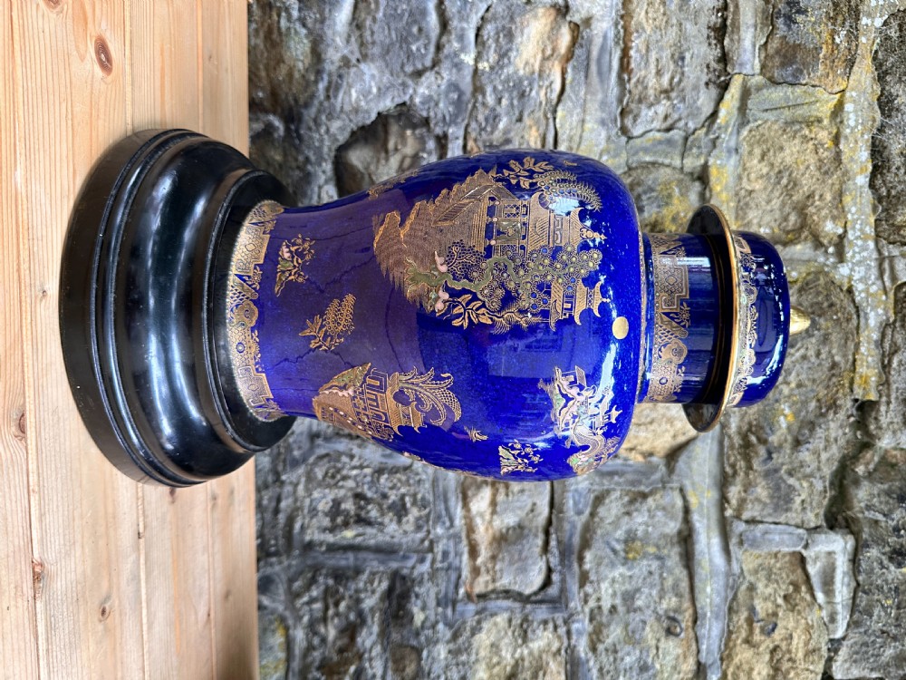 A pair of cobalt blue ceramic lidded vases decorated with gold gilt Chinoiserie pagoda scenes, set on dark circular ebonised wooden bases. View XI