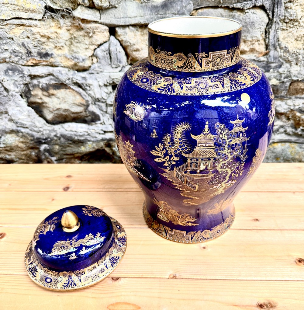 A pair of cobalt blue ceramic lidded vases decorated with gold gilt Chinoiserie pagoda scenes, set on dark circular ebonised wooden bases. View XII