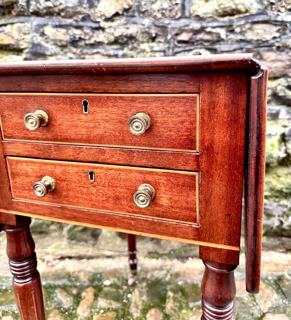 A Regency mahogany drop leaf side table featuring two drawers with brass knobs, boxwood string inlay, turned legs, and brass castors. View IV