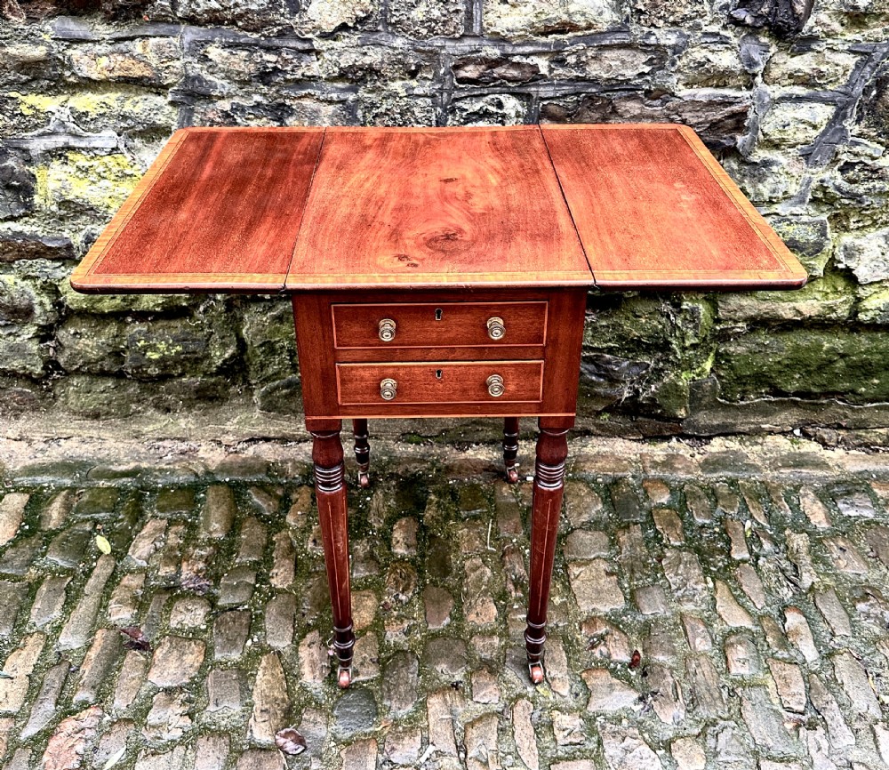 A Regency mahogany drop leaf side table featuring two drawers with brass knobs, boxwood string inlay, turned legs, and brass castors. View VII