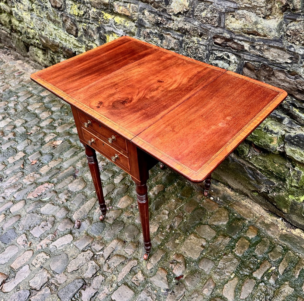 A Regency mahogany drop leaf side table featuring two drawers with brass knobs, boxwood string inlay, turned legs, and brass castors. View IX