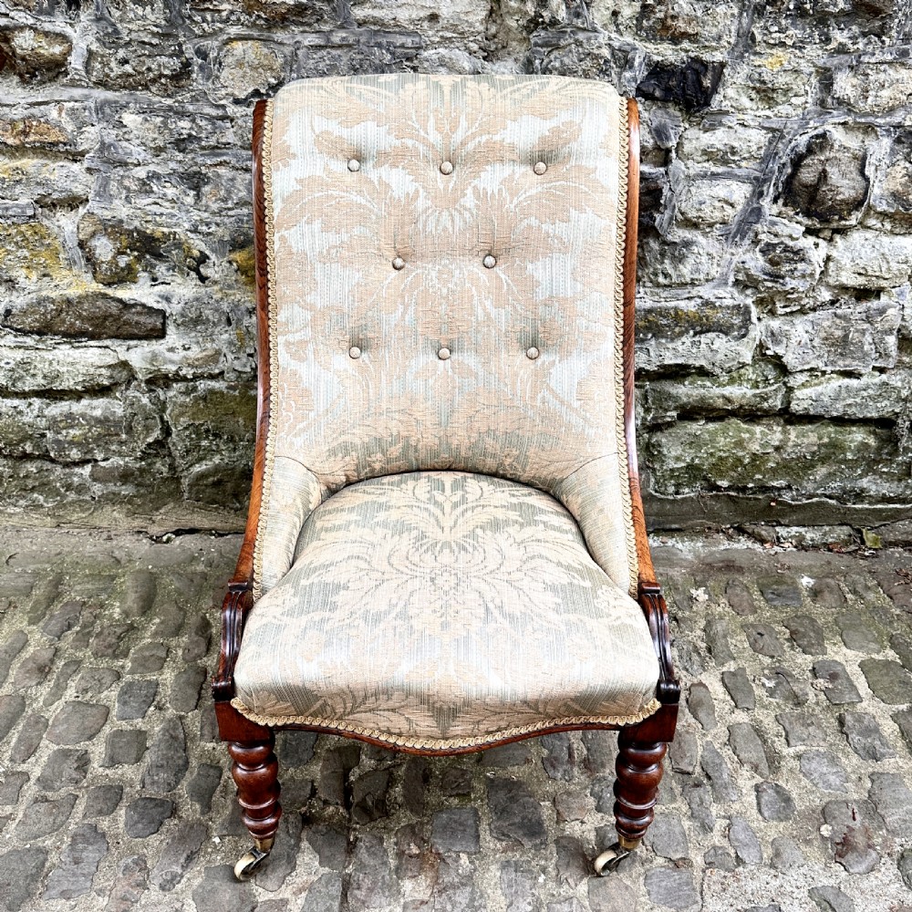 A William IV rosewood nursing chair upholstered in beige damask fabric with button-back detailing and turned front legs on brass castors.