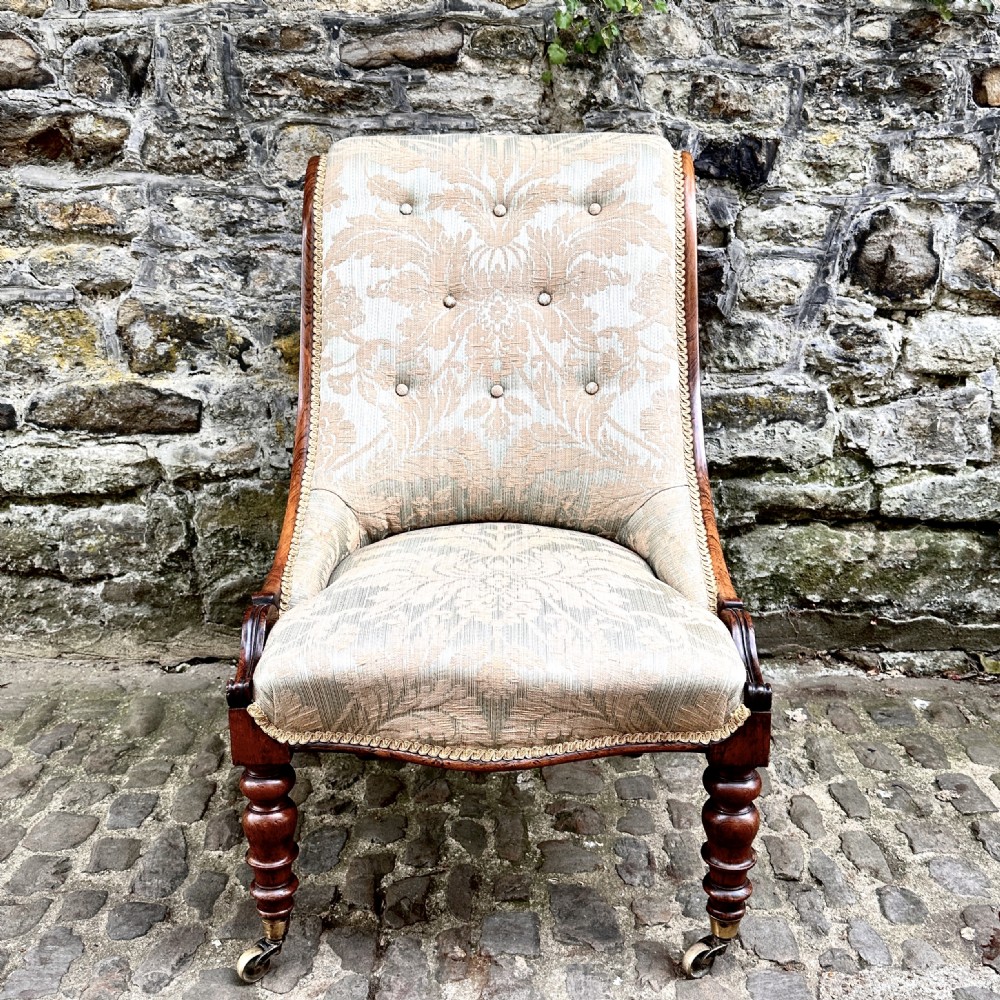 A William IV rosewood nursing chair upholstered in beige damask fabric with button-back detailing and turned front legs on brass castors. View II