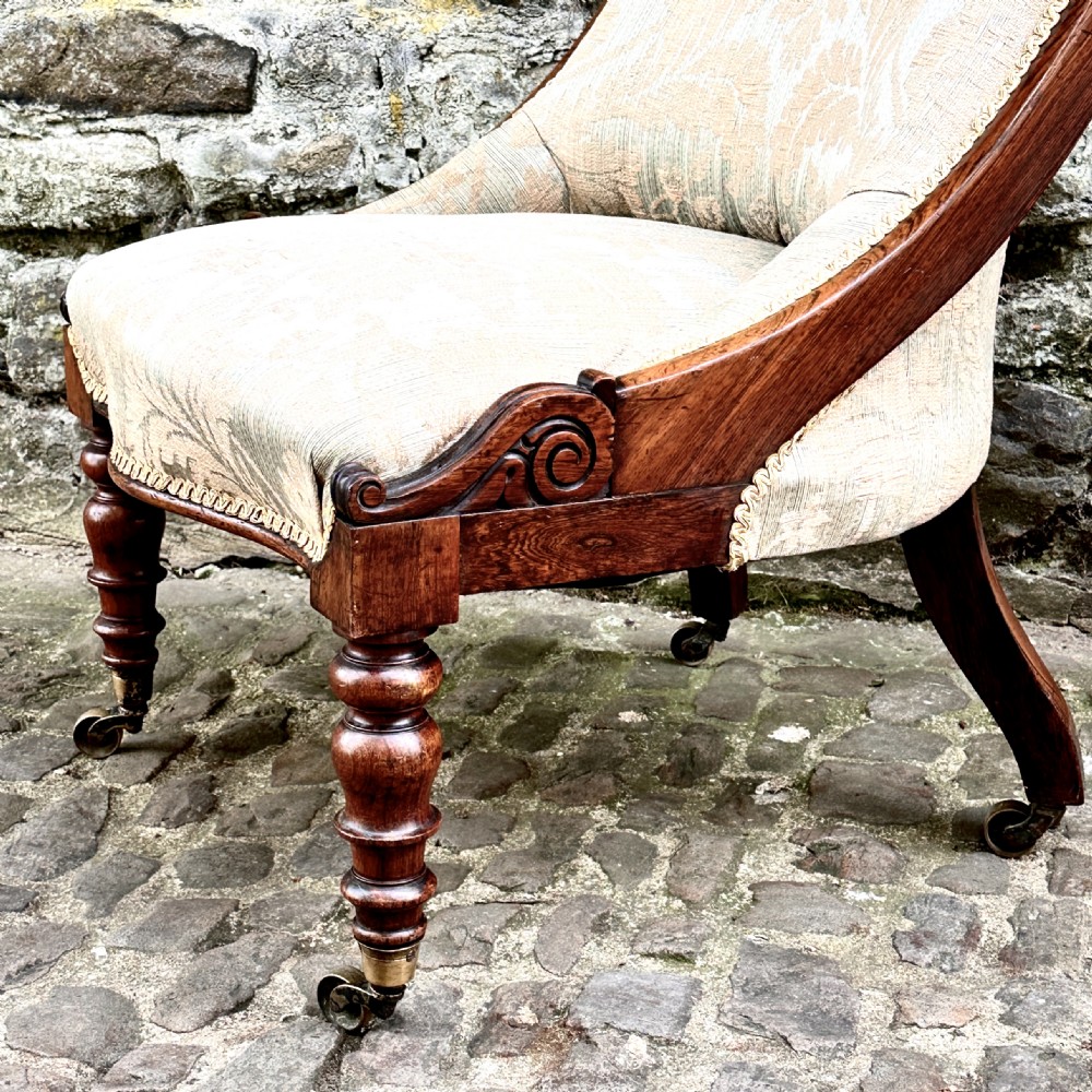 A William IV rosewood nursing chair upholstered in beige damask fabric with button-back detailing and turned front legs on brass castors. View IV
