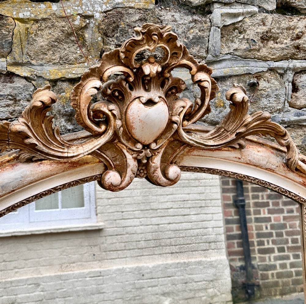 Mid 19th century arched French overmantel mirror with carved cartouche scroll cresting and a distressed cream and gold finish. View II
