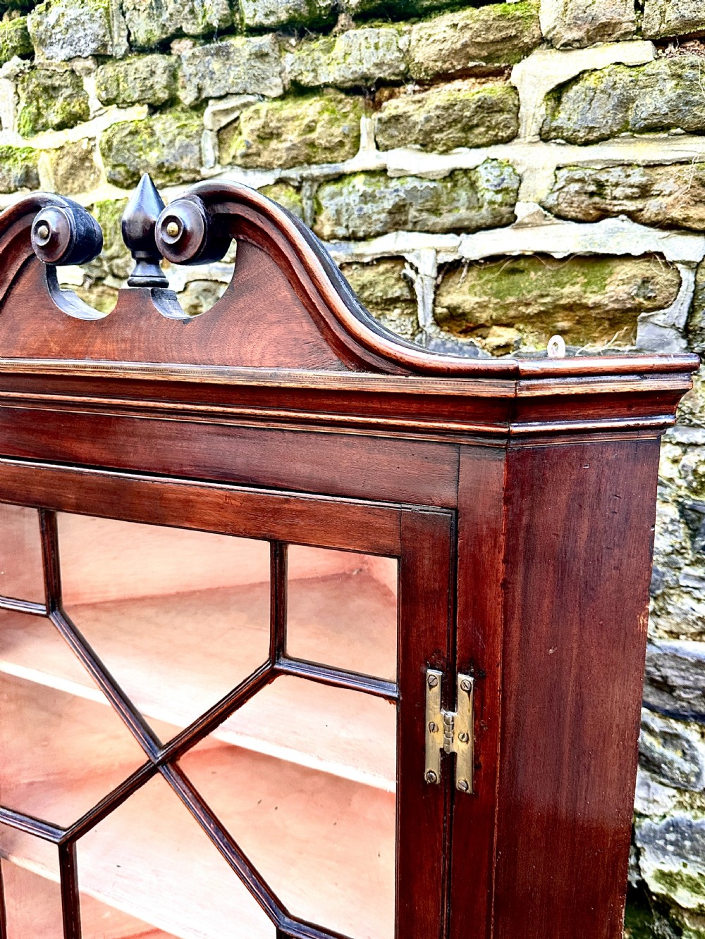 A George III mahogany corner cupboard featuring a glazed door with geometric astragal bars, a swan-neck pediment with a central finial, and brass H-hinges. View II