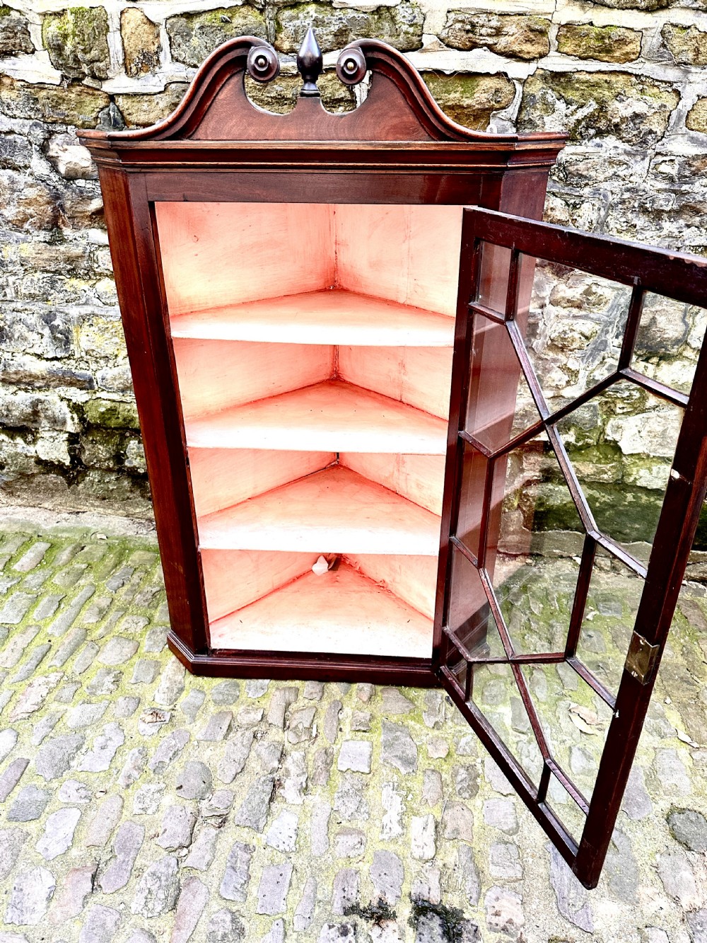 A George III mahogany corner cupboard featuring a glazed door with geometric astragal bars, a swan-neck pediment with a central finial, and brass H-hinges. View IV
