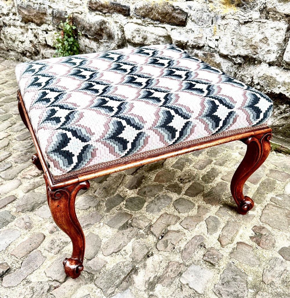 An Early Victorian walnut footstool with curved cabriole legs and patterned geometric upholstery. View V