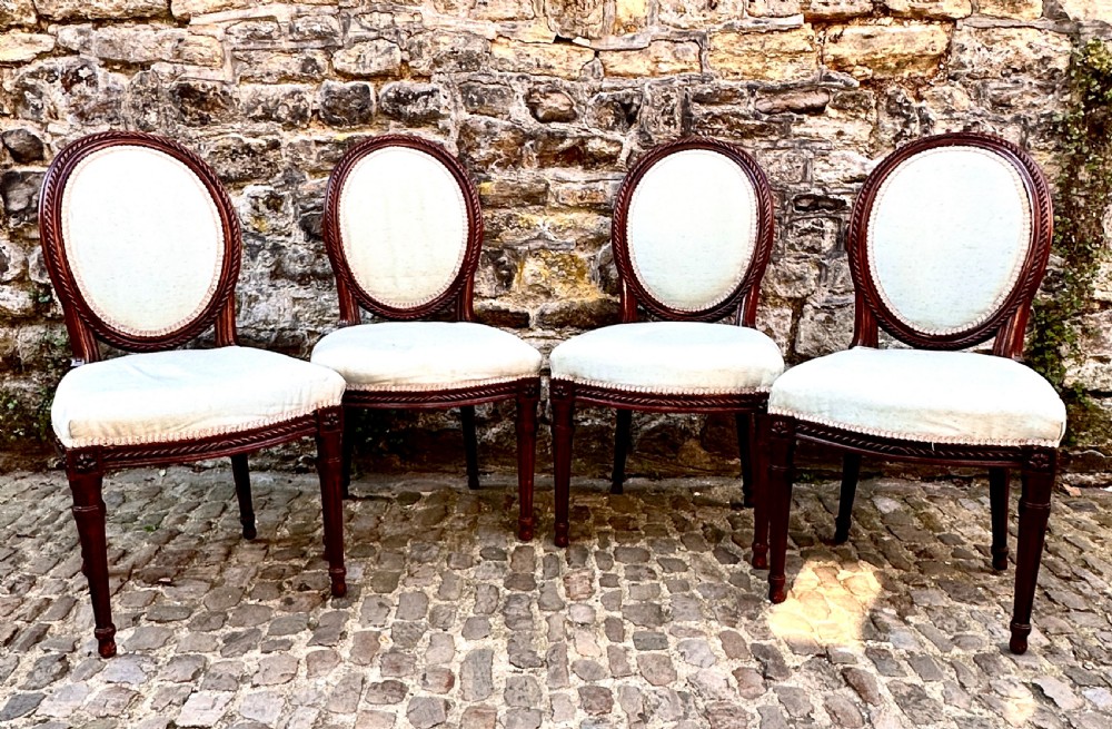 A set of four George III mahogany side chairs with oval upholstered backs, rope-twist carved borders, and fluted turned legs.