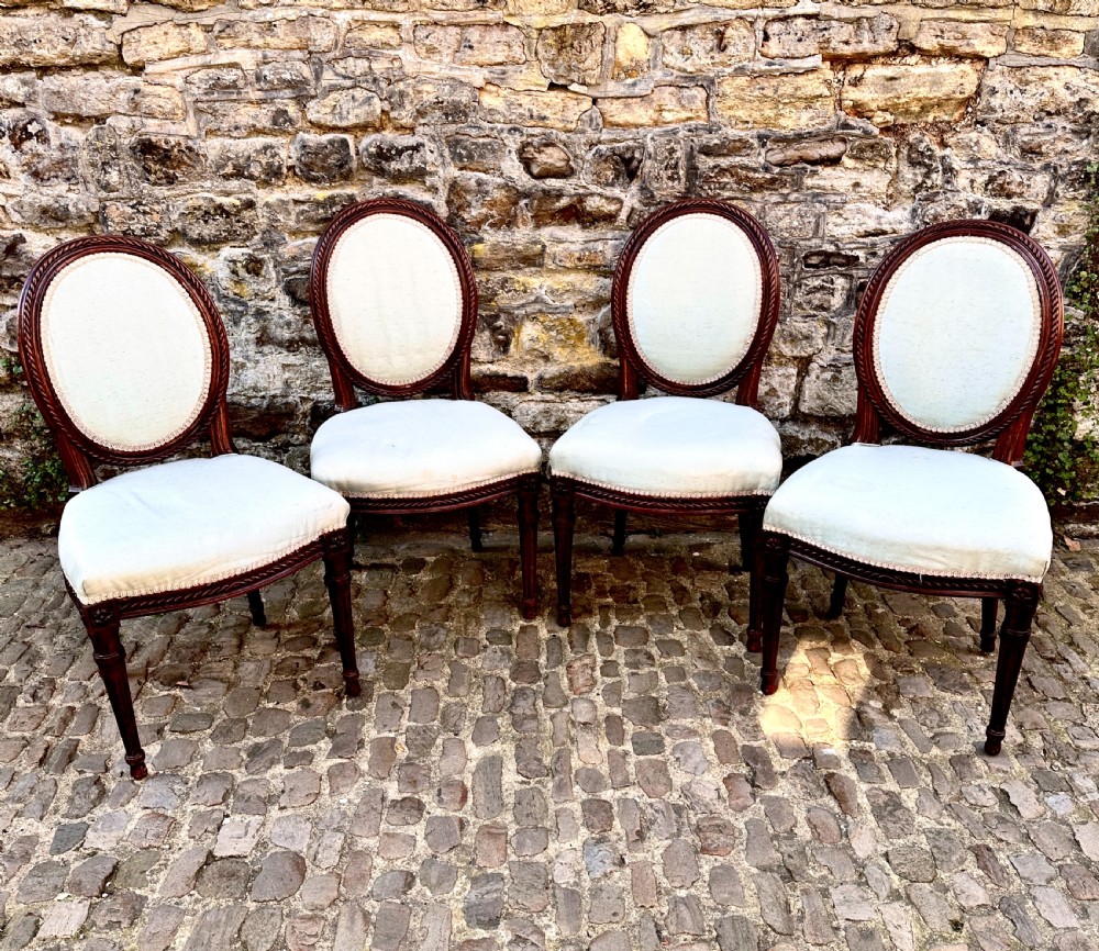 A set of four George III mahogany side chairs with oval upholstered backs, rope-twist carved borders, and fluted turned legs. View X