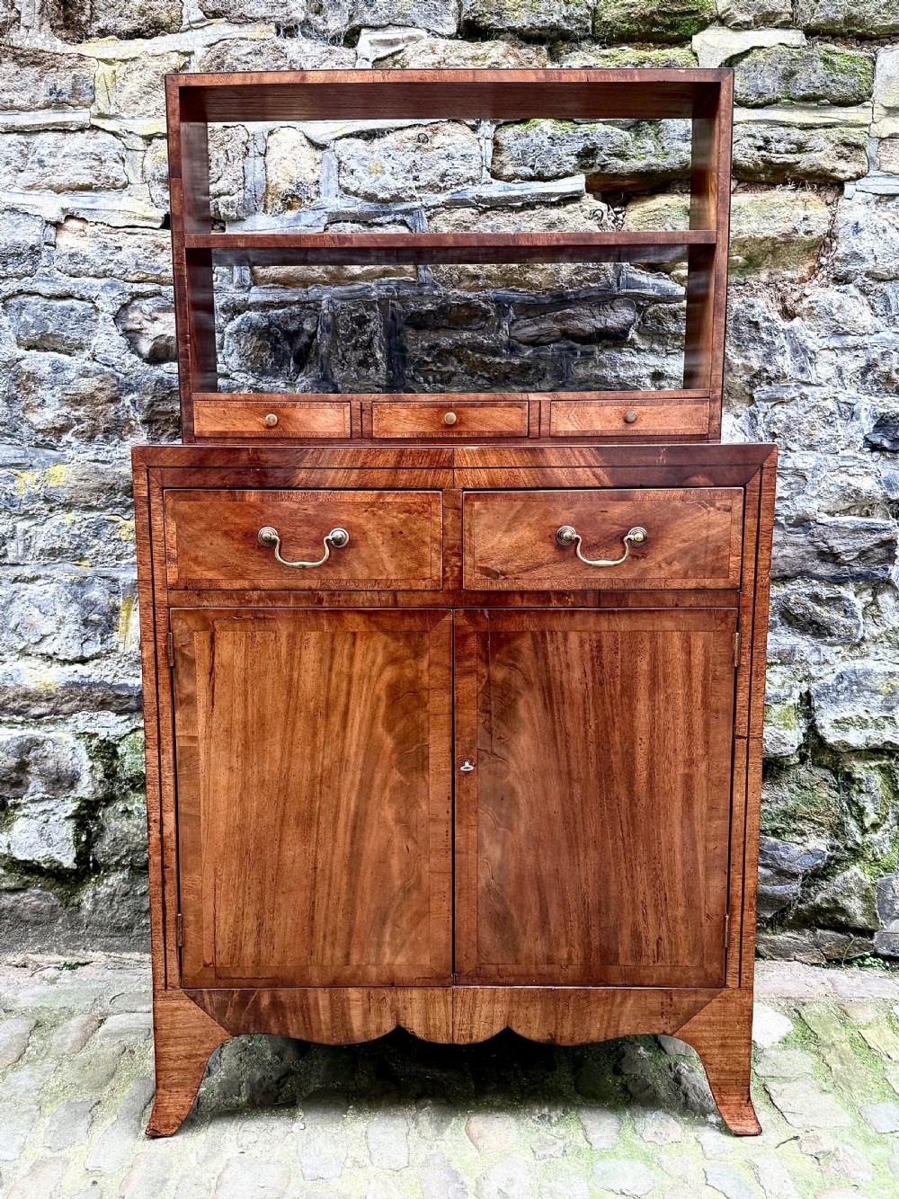 A George III mahogany chiffonier featuring a top open shelf unit with three small drawers above a two-drawer base cabinet with panelled doors and curved feet.