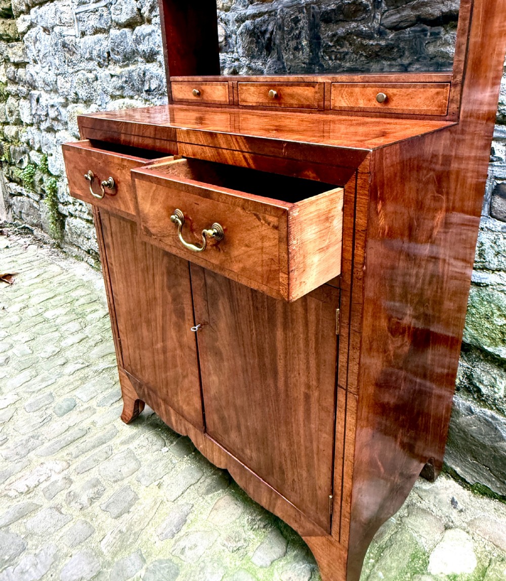 A George III mahogany chiffonier featuring a top open shelf unit with three small drawers above a two-drawer base cabinet with panelled doors and curved feet. View IV