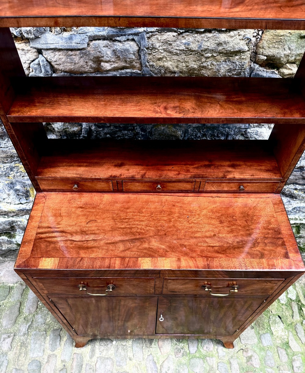 A George III mahogany chiffonier featuring a top open shelf unit with three small drawers above a two-drawer base cabinet with panelled doors and curved feet. View VI