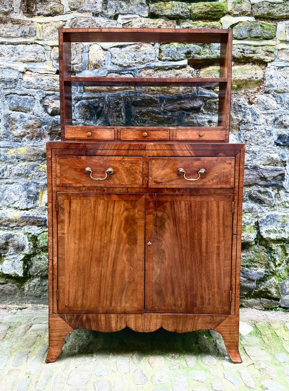 A George III mahogany chiffonier featuring a top open shelf unit with three small drawers above a two-drawer base cabinet with panelled doors and curved feet. View VII