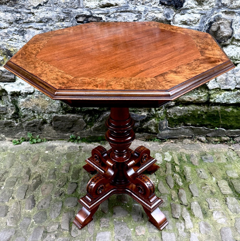 An octagonal mid-Victorian centre table crafted from walnut with a veneered top, turned pedestal stem, and carved four-legged scroll base.