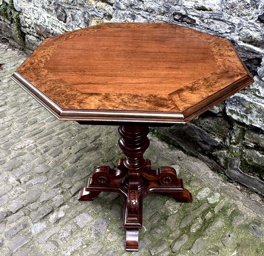 An octagonal mid-Victorian centre table crafted from walnut with a veneered top, turned pedestal stem, and carved four-legged scroll base. View VI