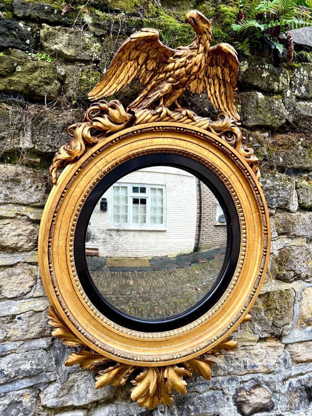 A circular Regency giltwood convex mirror topped with a carved eagle crest and framed with an ebonised inner ring.