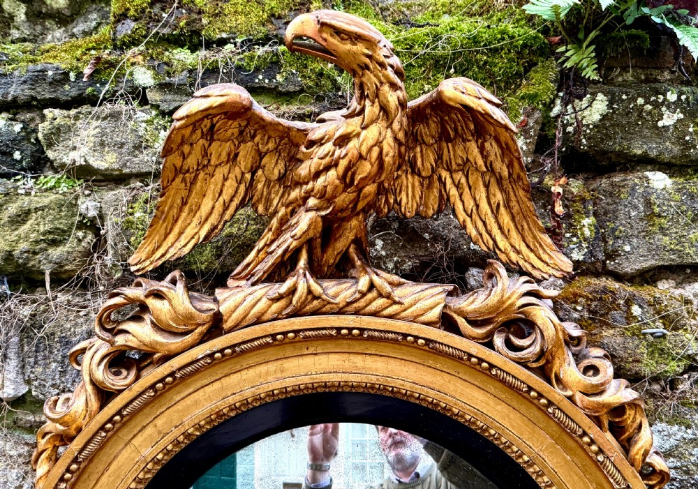 A circular Regency giltwood convex mirror topped with a carved eagle crest and framed with an ebonised inner ring. View II