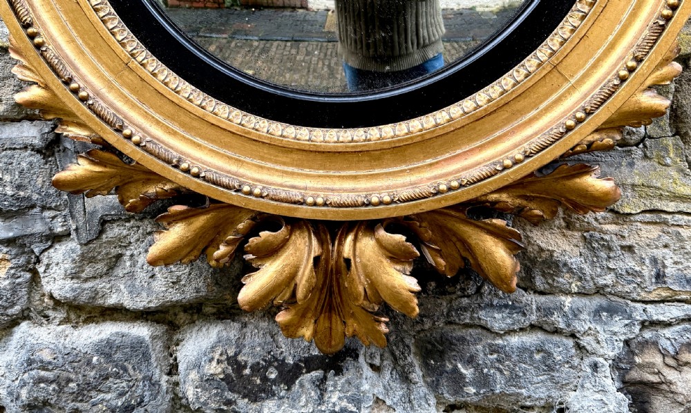 A circular Regency giltwood convex mirror topped with a carved eagle crest and framed with an ebonised inner ring. View III