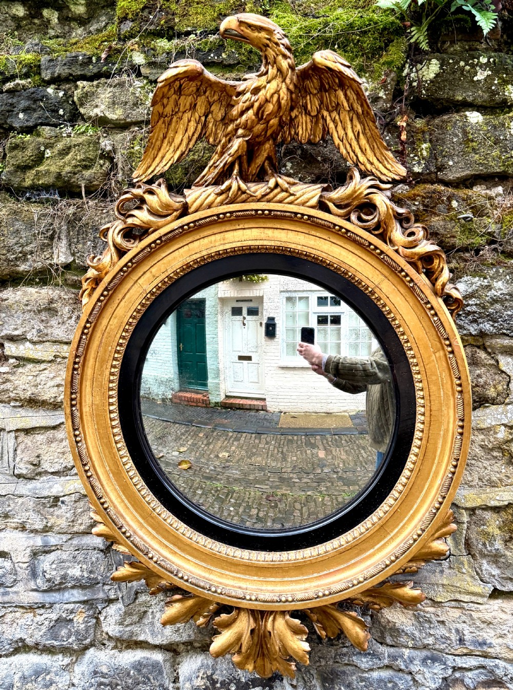 A circular Regency giltwood convex mirror topped with a carved eagle crest and framed with an ebonised inner ring. View VI