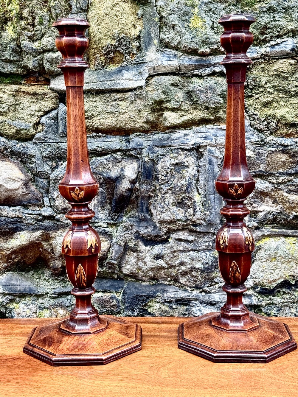 A pair of turned Adam style mahogany candlesticks featuring carved leaf detailing and octagonal bases.