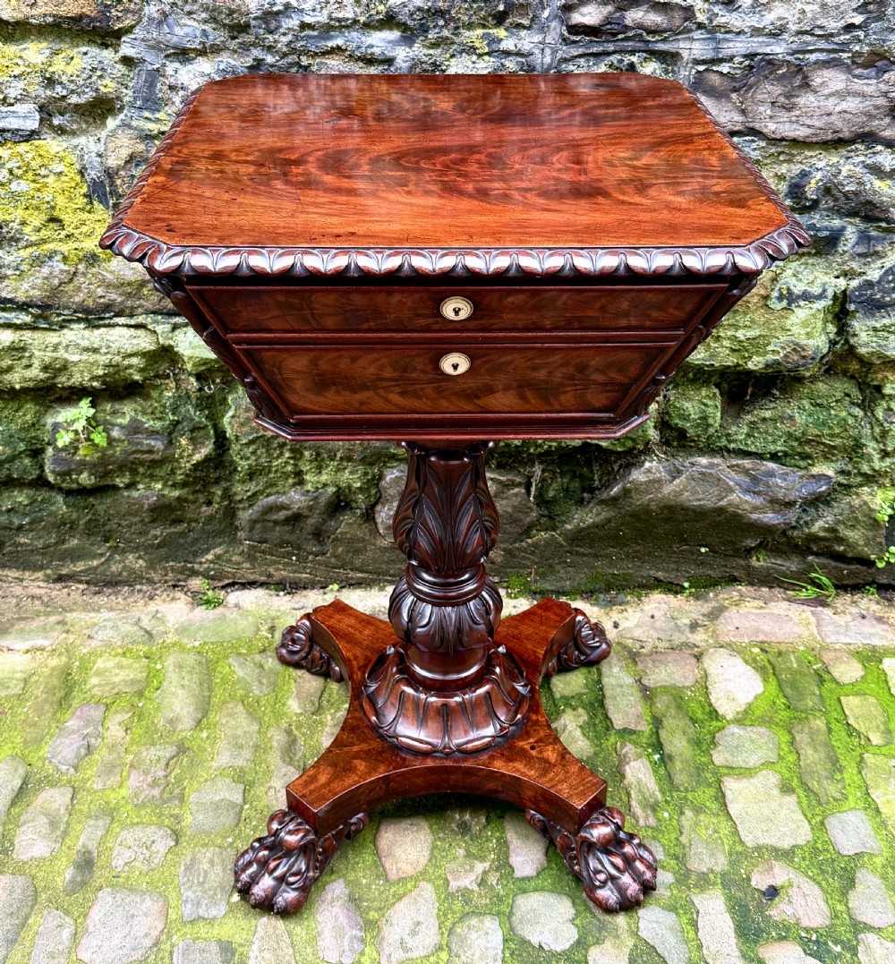 A William IV flame mahogany work table featuring a gadrooned top edge, two drawers with bone escutcheons, a carved pedestal stem, and a quadform base with claw feet.