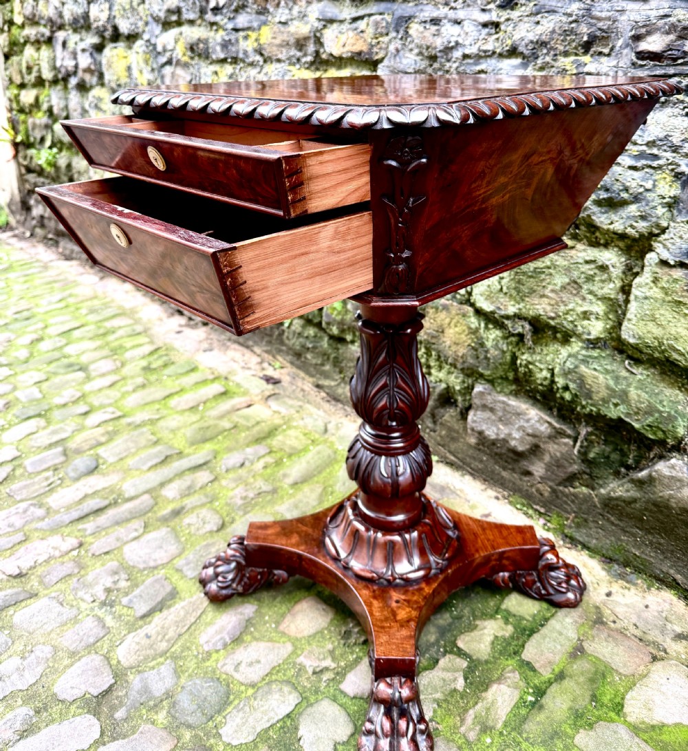 A William IV flame mahogany work table featuring a gadrooned top edge, two drawers with bone escutcheons, a carved pedestal stem, and a quadform base with claw feet. View IX