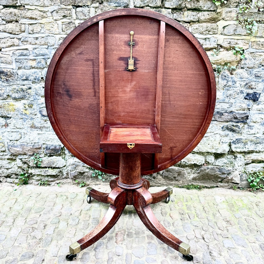 A circular George III burr yew wood pedestal centre table shown tilted vertically on downswept legs with brass castors. View IV