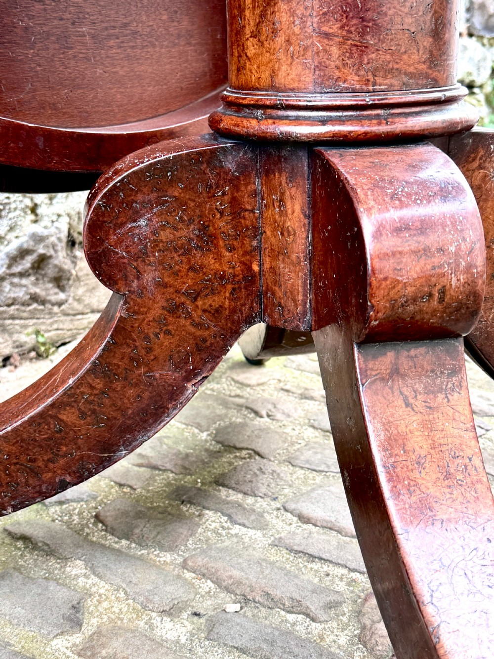 A circular George III burr yew wood pedestal centre table shown tilted vertically on downswept legs with brass castors. View VI