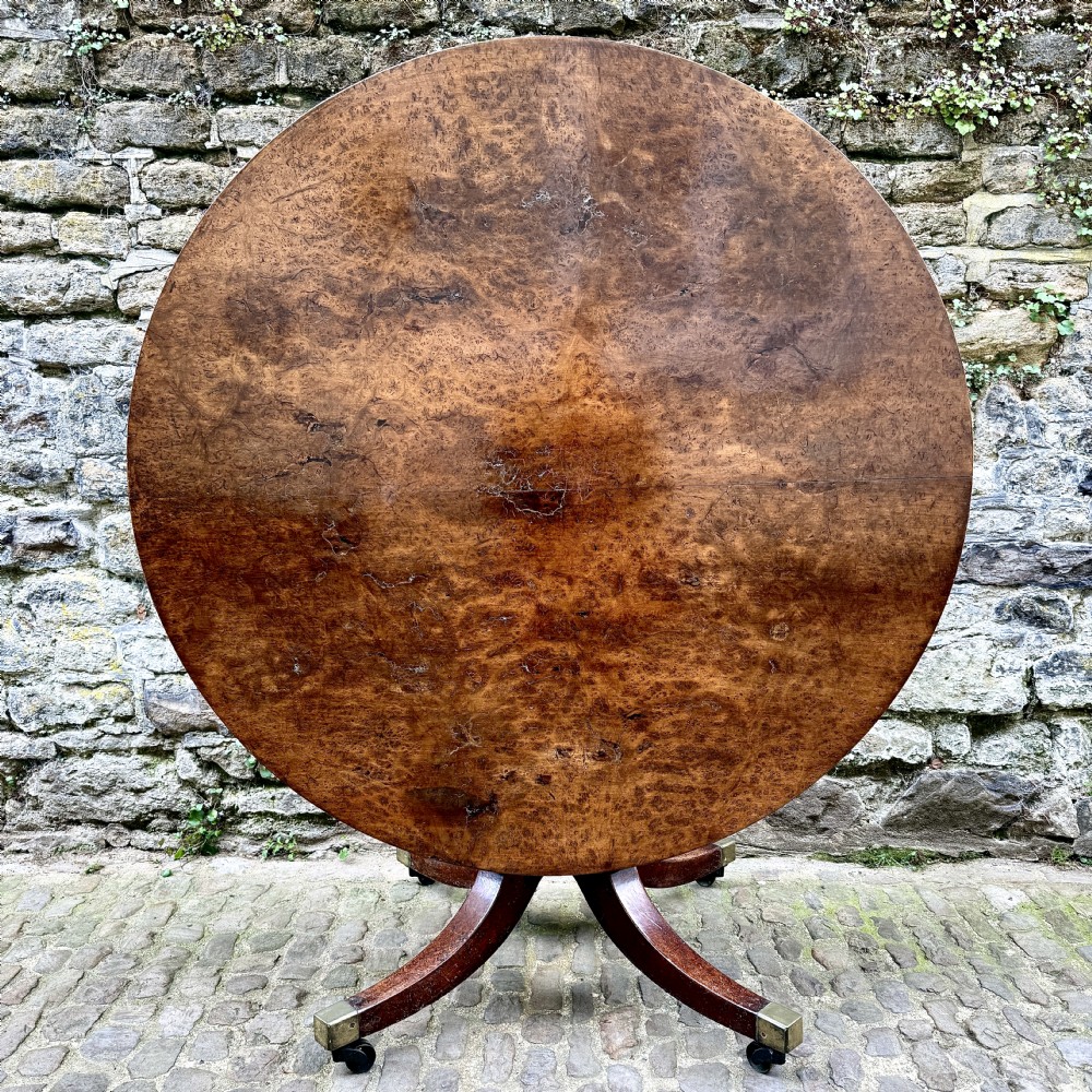 A circular George III burr yew wood pedestal centre table shown tilted vertically on downswept legs with brass castors. View XII