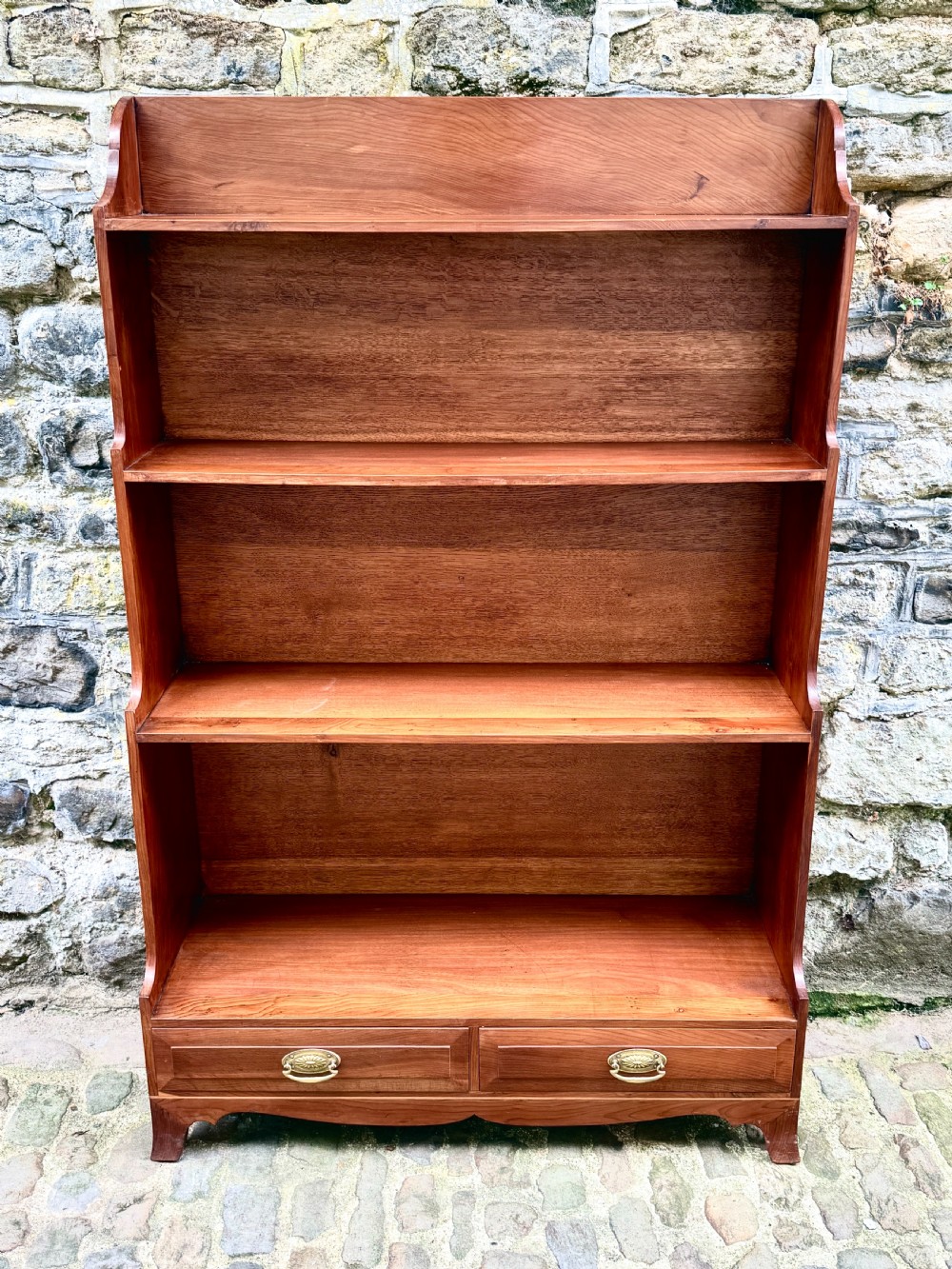 An early twentieth-century yew wood waterfall bookcase featuring four graduated open shelves above two drawers with brass handles.