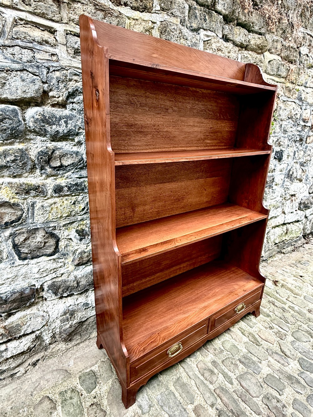 An early twentieth-century yew wood waterfall bookcase featuring four graduated open shelves above two drawers with brass handles. View VII
