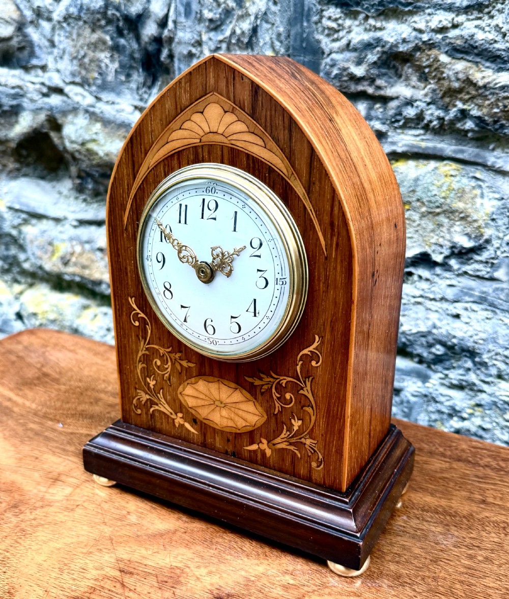 A lancet-arched wooden mantel clock featuring marquetry floral inlays, a white enamel dial, and a brass bezel. View II