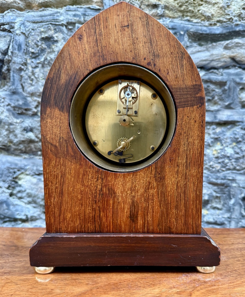 A lancet-arched wooden mantel clock featuring marquetry floral inlays, a white enamel dial, and a brass bezel. View III