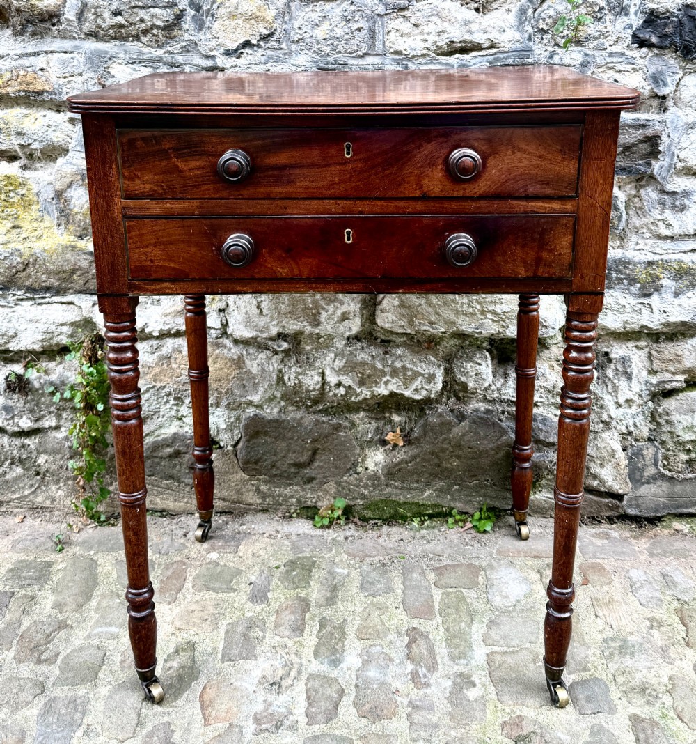 A Regency mahogany side table featuring two drawers with turned wooden handles, ring-turned legs, and brass castors.