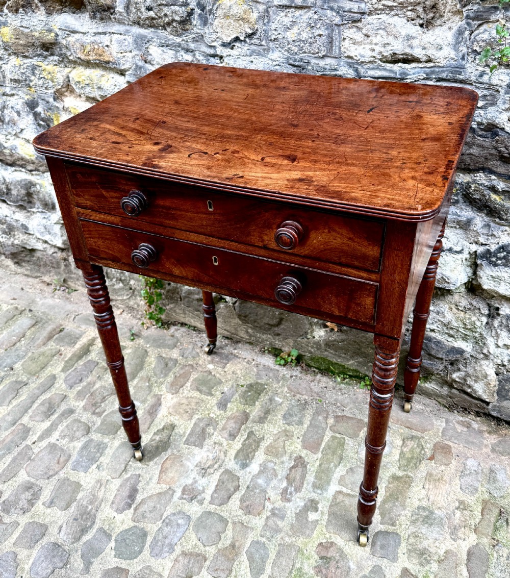 A Regency mahogany side table featuring two drawers with turned wooden handles, ring-turned legs, and brass castors. View II