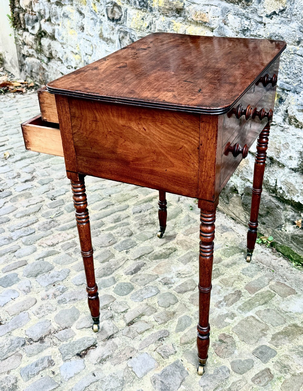 A Regency mahogany side table featuring two drawers with turned wooden handles, ring-turned legs, and brass castors. View V