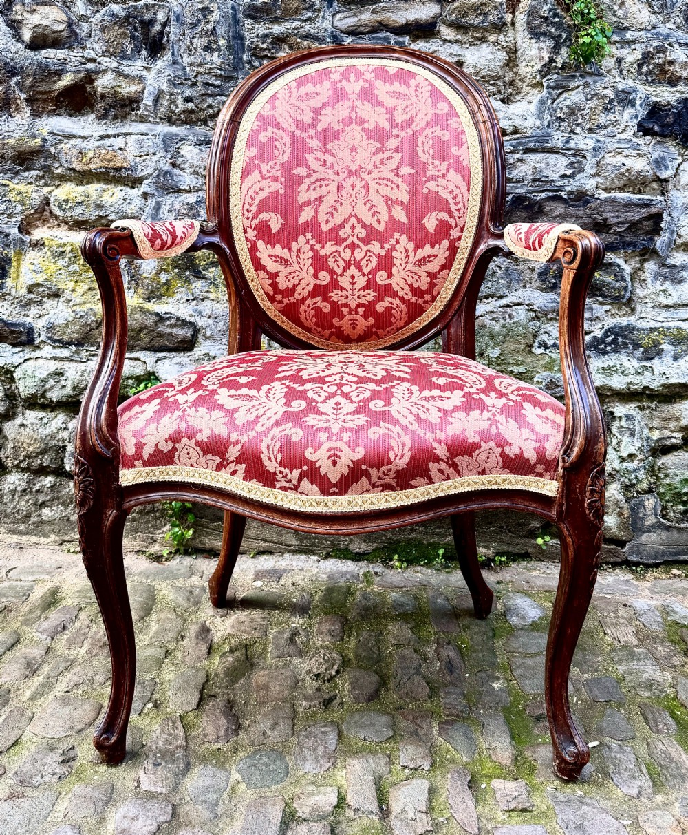 A French Louis XV style open-arm chair crafted from carved walnut with red and gold damask upholstery.
