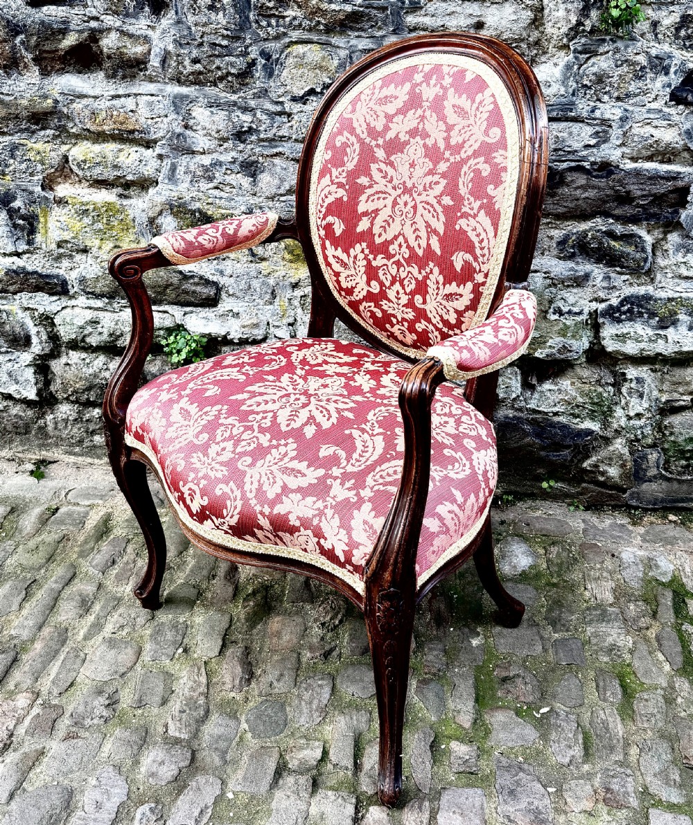 A French Louis XV style open-arm chair crafted from carved walnut with red and gold damask upholstery. View IV