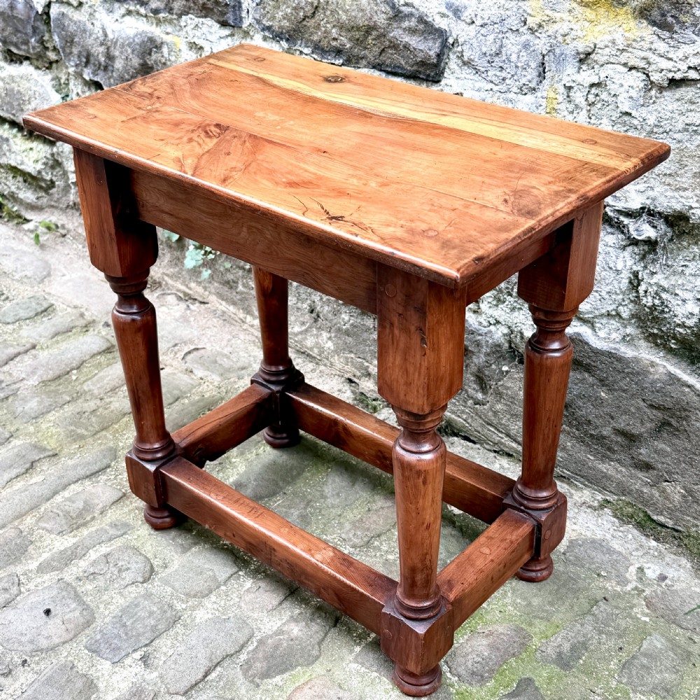 A pair of warm brown yew wood joint stools with rectangular tops, turned legs, and square perimeter stretchers resting on a cobblestone floor. View IX